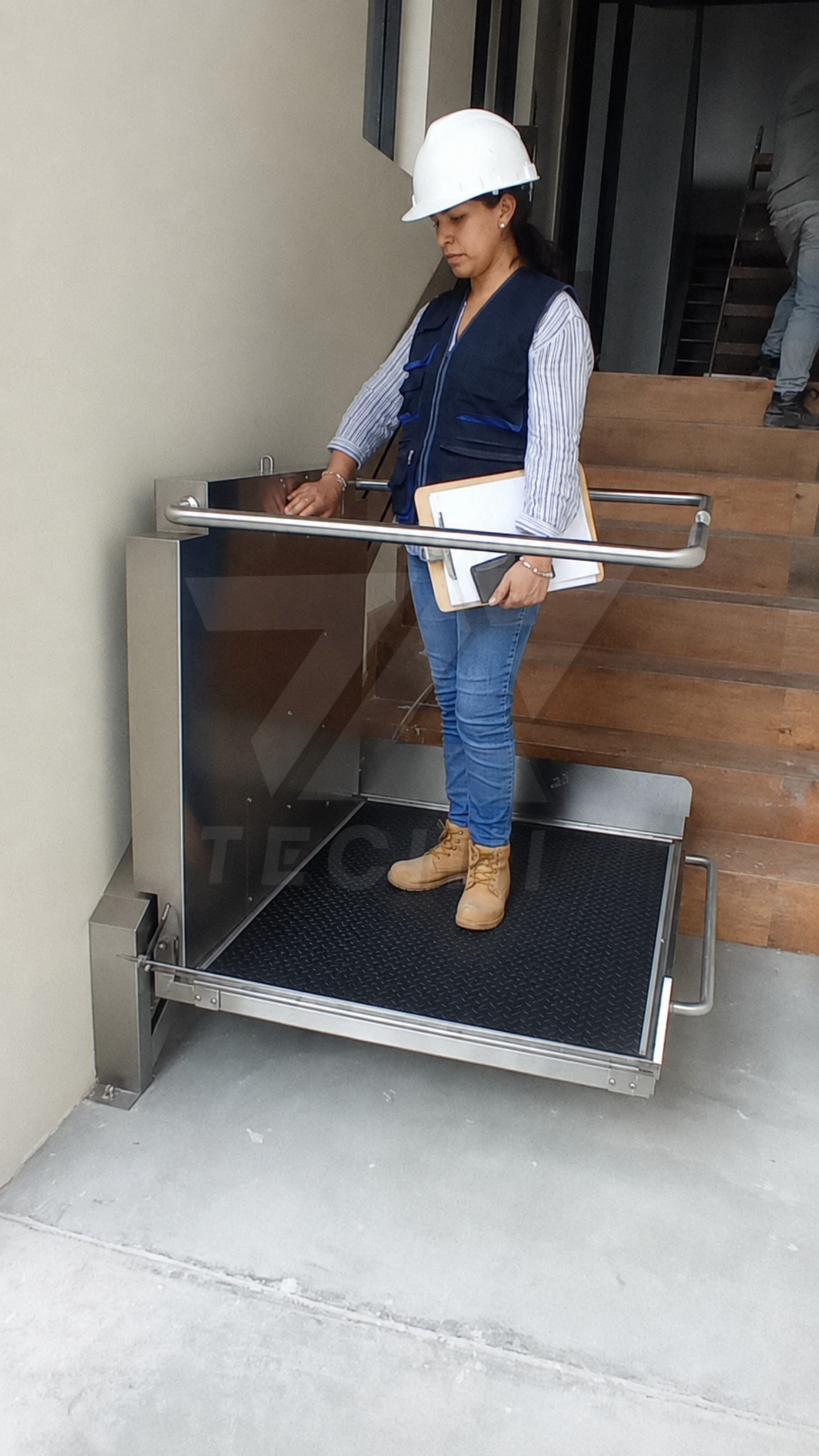 Plataforma salvaescalera vertical TECINI para personas con movilidad reducida instalada junto a una escalera interior.